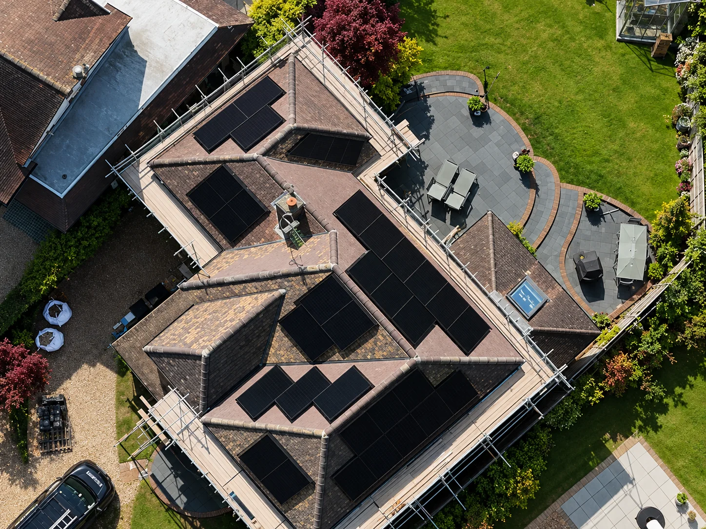 Aerial view of a large tiled-roof house with black solar panels installed across several roof slopes and scaffolding in place