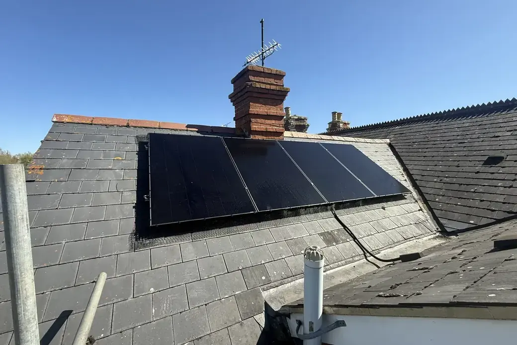 Completed black solar array on a slate roof beside a chimney stack
