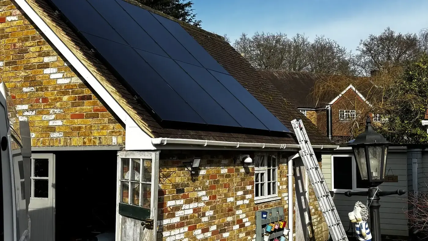 All-black solar panels on the roof of a brick and flint cottage